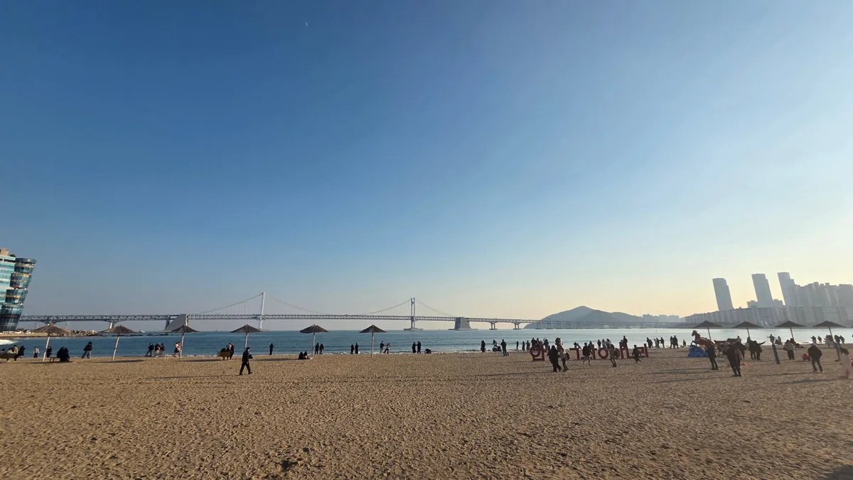 넓은 광안리 모래사장을 산책하는 사람들과 광안대교, 오른쪽의 해운대 쪽 고층 빌딩
