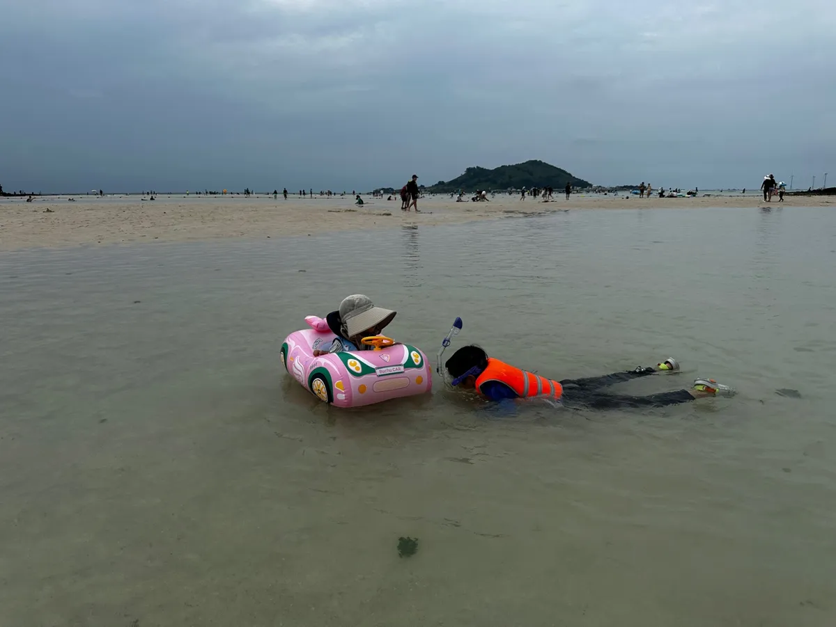 협재해수욕장 얕은 바다에서 튜브를 탄 아이와 스노클링하는 아이, 뒤로 보이는 비양도