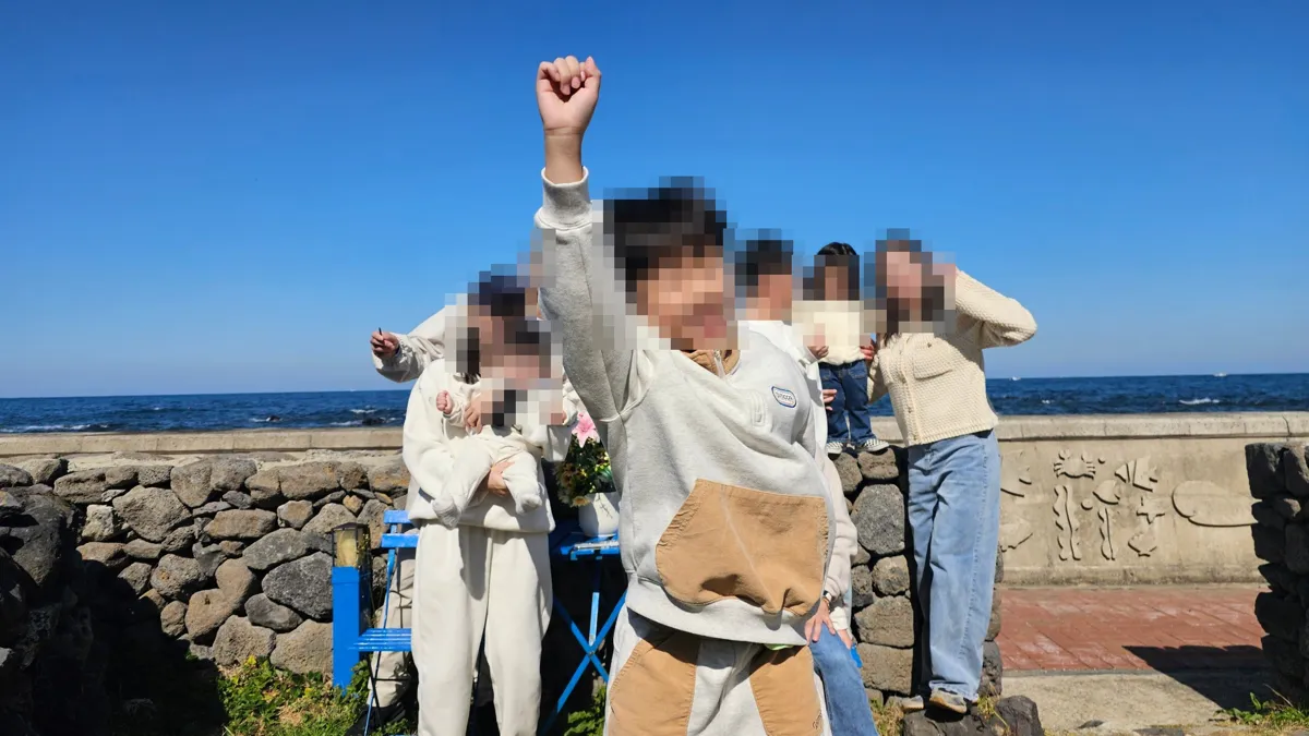 제주 바닷가 돌담 앞에서 즐겁게 사진을 찍는 가족, 얼굴은 모자이크 처리