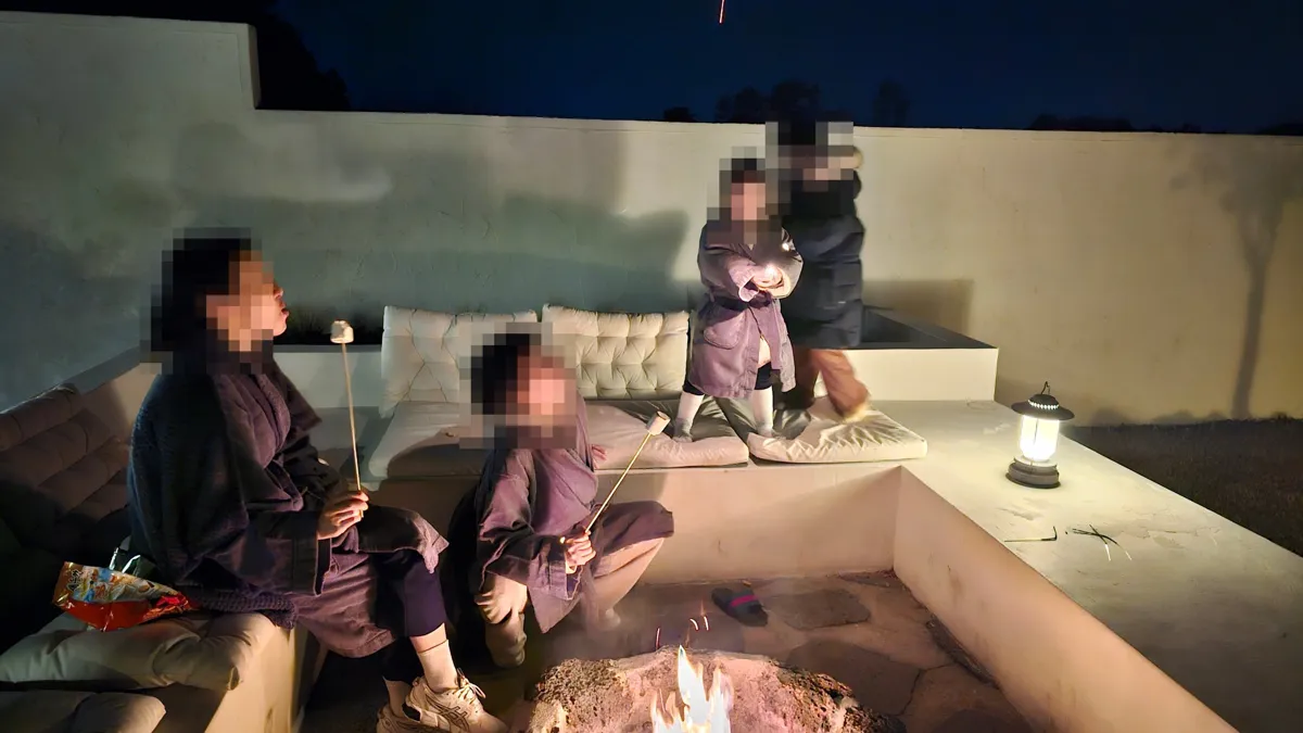 화롯가에 둘러앉아 마시멜로를 굽는 가족과 불꽃놀이를 하는 아이들, 얼굴은 모자이크 처리