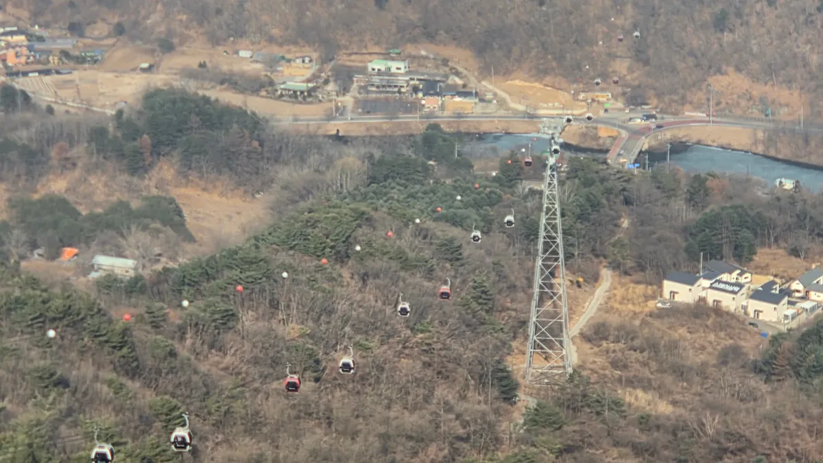 위에서 내려다본 산비탈을 따라 줄지어 오르내리는 빨간색과 흰색 케이블카 캐빈과 철탑