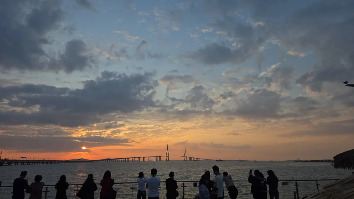 송도 해안 공원 난간에 모여 인천대교 너머로 지는 해를 바라보는 사람들